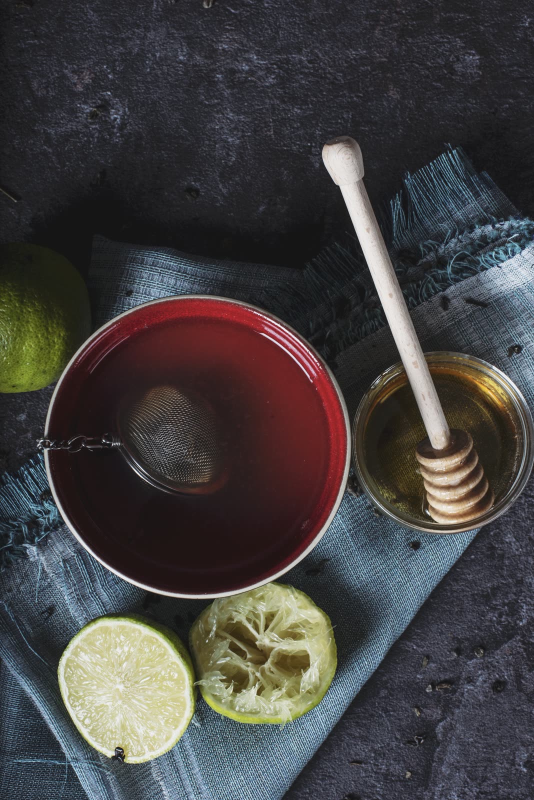 Xícara de chá vermelho com infusor, mel e limão sobre um pano azul