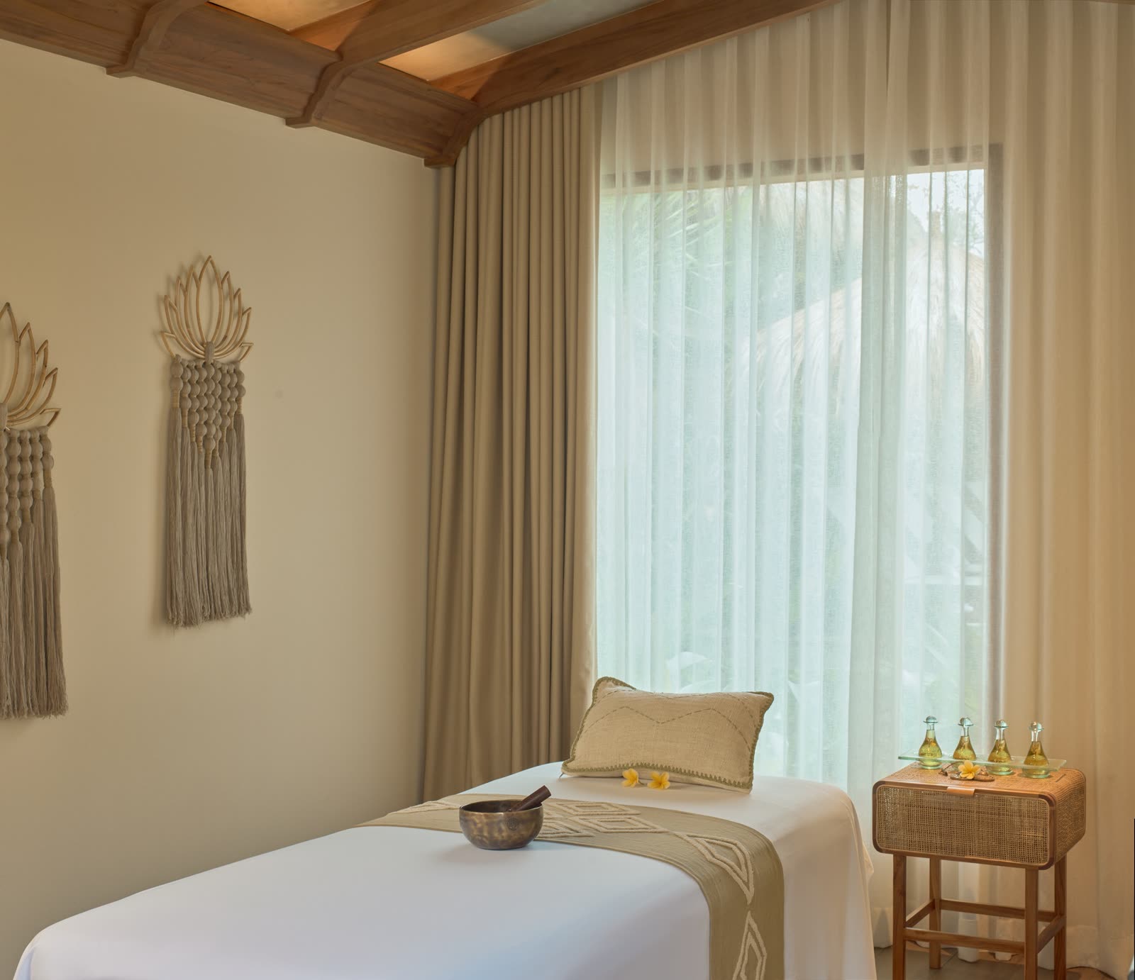 Sala de massagem com maca, cortina clara e frascos de óleo numa mesinha